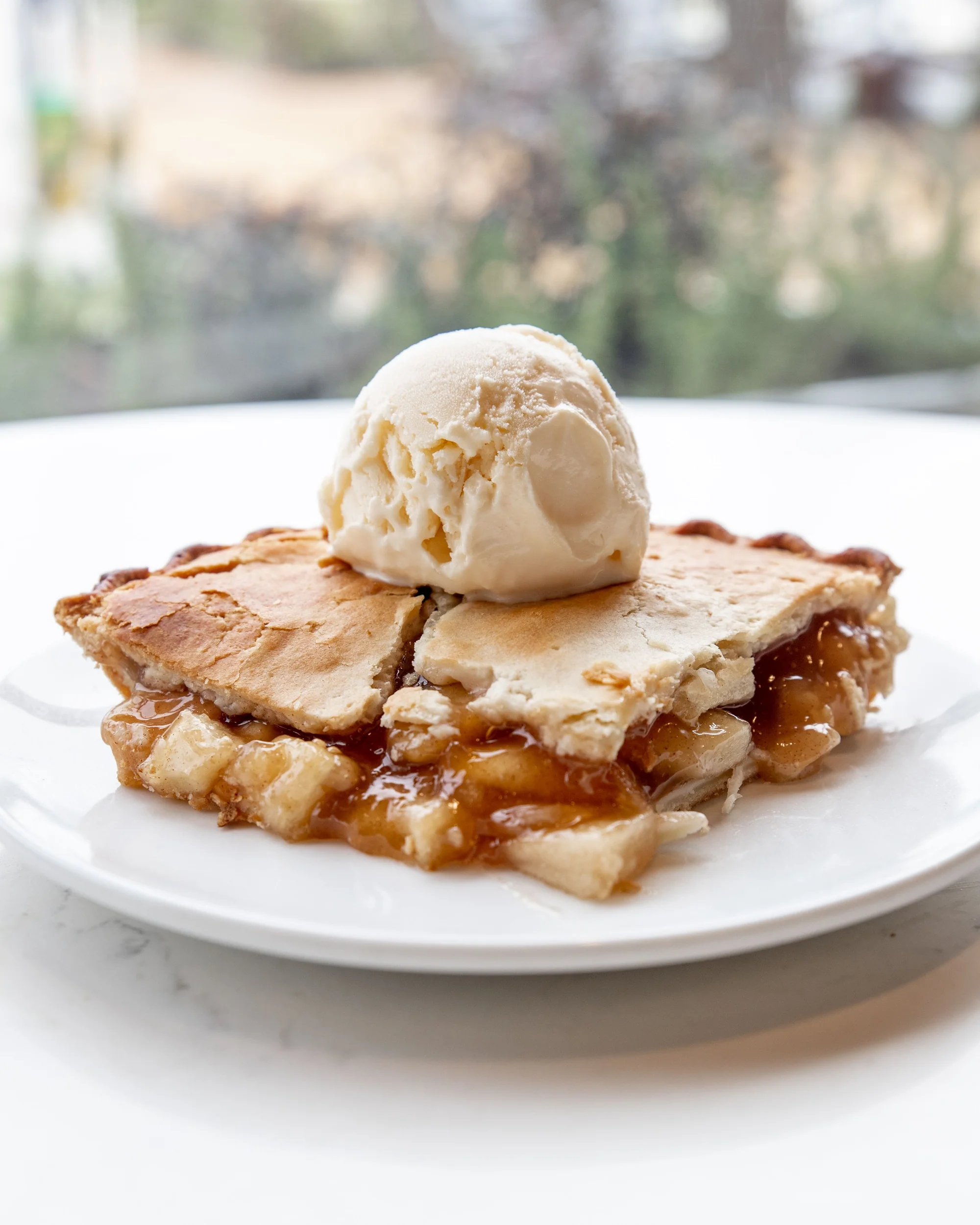 Slice of apple pie on a white plate topped with a scoop of vanilla ice cream